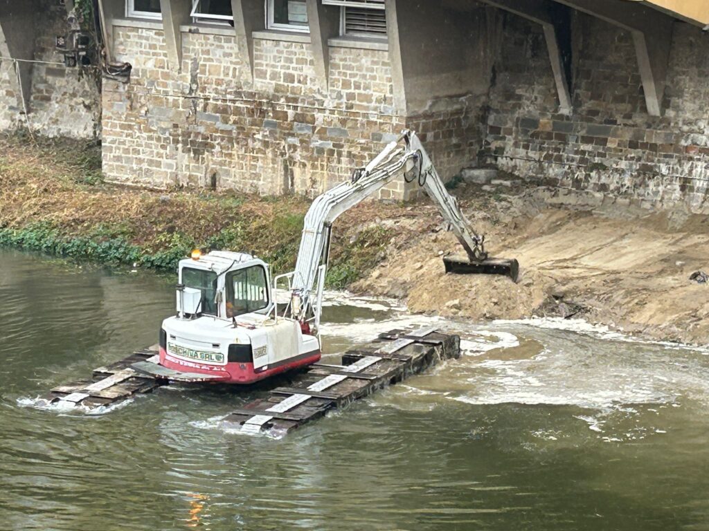 Escavatore anfibio in azione sull’Arno nel centro di Firenze per la manutenzione delle sponde